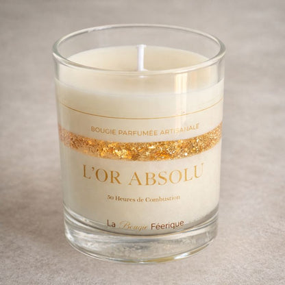 Bougie Parfumée Artisanale L’Or Absolu dans verre transparent, cire blanche avec feuilles d’or scintillantes, design élégant sur fond neutre beige, ambiance luxe et raffinée.