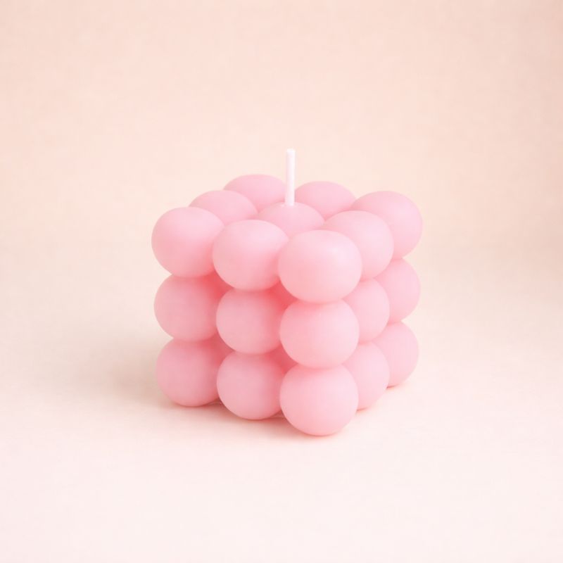 Bougie Parfumée Cube Design, de couleur rose et de forme bubble carré. Sur fond beige clair.