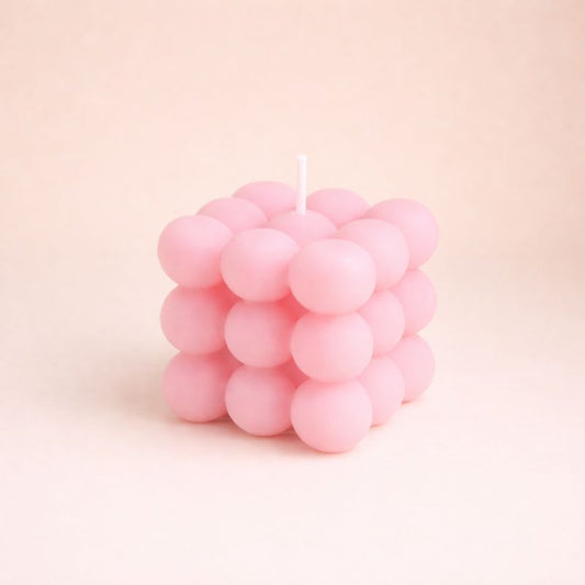 Bougie Parfumée Cube Design, de couleur rose et de forme bubble carré. Sur fond beige clair.