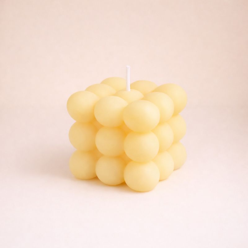 Bougie Parfumée Cube Design, de couleur jaune et de forme bubble carré. Sur fond beige clair.