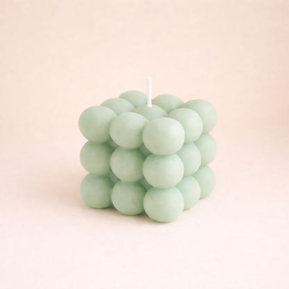 Bougie Parfumée Cube Design, de couleur verte et de forme carré bubble. Sur fond beige clair.