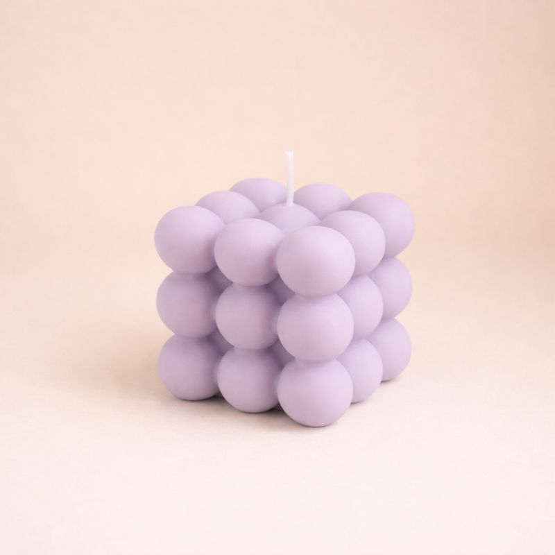 Bougie Parfumée Cube Design, de couleur violette et de forme bubble carré. Sur fond beige clair.