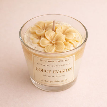 Bougie parfumée Douce Évasion en verre avec fleurs sculptées à la main et parfum fleur d’oranger ambiance cocooning élégante et chaleureuse. Sur fond beige clair.