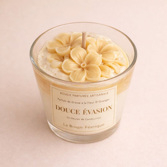 Bougie parfumée Douce Évasion en verre avec fleurs sculptées à la main et parfum fleur d’oranger ambiance cocooning élégante et chaleureuse. Sur fond beige clair.