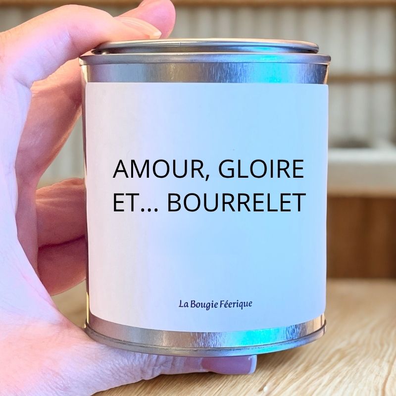 Bougie Personnalisée "Amour Gloire et Bourrelet", la bougie est maintenue dans une main d'humain et posée sur un plan de travail en bois.