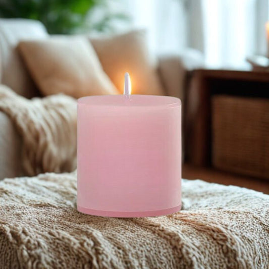 Bougie Pilier Rose Dragée, de couleur rose posée sur un plaid, dans une ambiance cocooning.