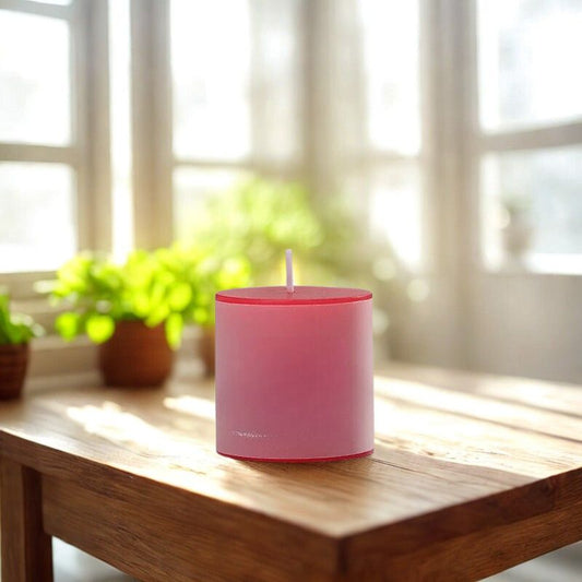 Bougie Pilier Rouge Passion, posée sur une table en bois et des plantes vertes en arrière-plan.