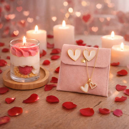 Bougie Saint Valentin Coffret Passion, il est pos sur une table en bois recouverte de pétales rouges, la bougie est allumée et les boucles d’oreilles ainsi que le collier sont posés sur la pochette rose. Ambiance romantique.