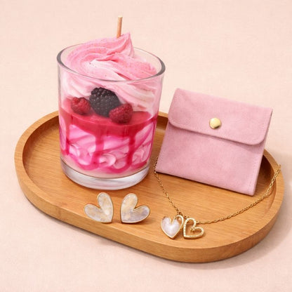Bougie Saint Valentin Coffret Tendre Moment, il se compose d'une bougie rose aux fruits rouges, d'une pochette rose, d'une parure de bijoux en forme de coeur, le tout sur un plateau en bois. Fond beige clair.