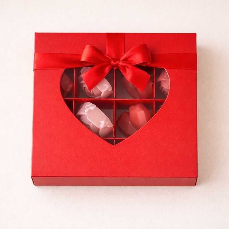 Bougie Saint Valentin Fondant Parfumé en Coffret Cadeau, de couleur rouge avec un noeud de la même couleur, avec un coeur transparent sur  et sur fond beige clair.