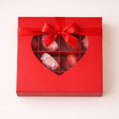 Bougie Saint Valentin Fondant Parfumé en Coffret Cadeau, de couleur rouge avec un noeud de la même couleur, avec un coeur transparent sur  et sur fond beige clair.