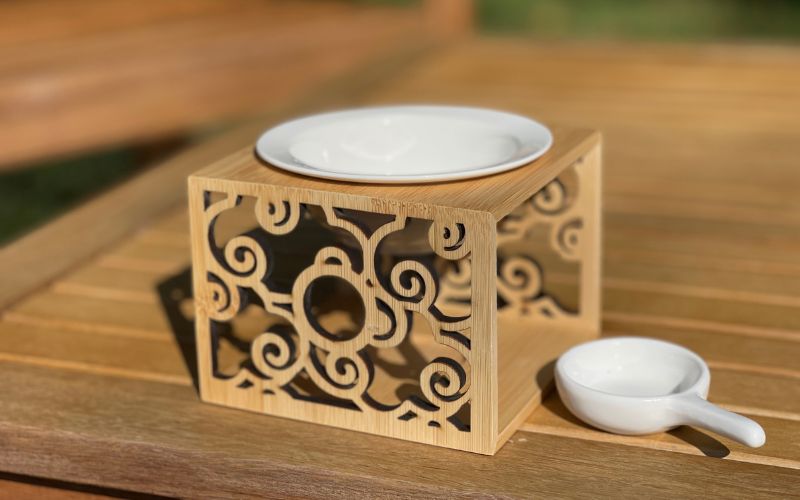 Brule Parfum en bois et céramique avec sa petite coupelle pour disposer la bougie chauffe-plat, le tout posé sur une table en bois.