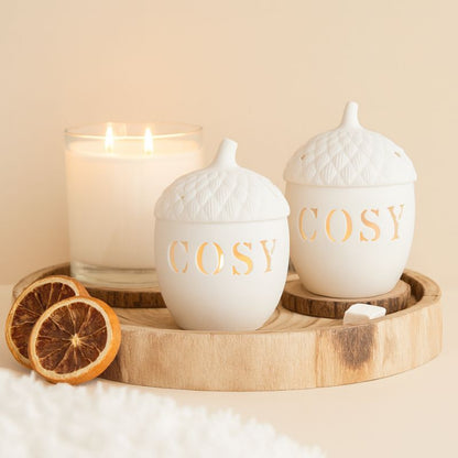 Brule Parfum Esprit Cocooning, on peut voir deux brûleurs identiques, avec une bougie d'allumer à côté, le tout est posé dans un plateau en bois, sur fond beige clair.