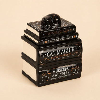 Brule Parfum Livre Magique Chat Noir en céramique noire et blanche au design livres empilés avec chat décoratif. Fond beige clair.