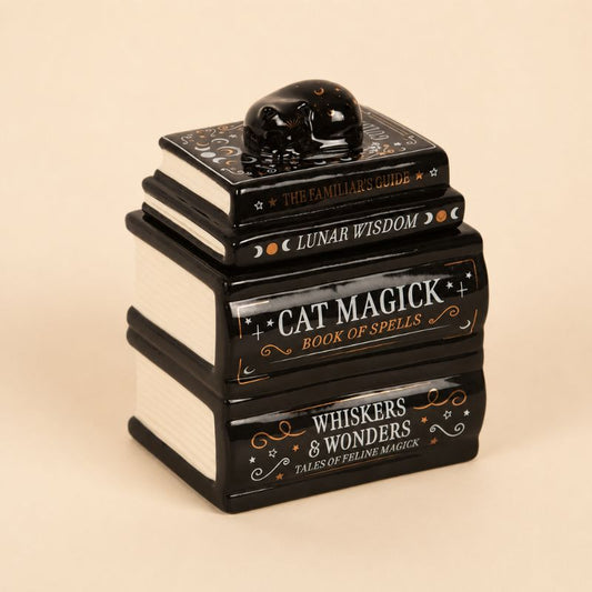 Brule Parfum Livre Magique Chat Noir en céramique noire et blanche au design livres empilés avec chat décoratif. Fond beige clair.