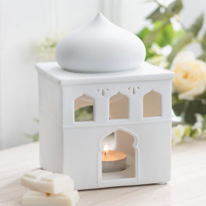 Brule Parfum Lueur d’Orient, le brûleur est allumé et il y a du fondant parfumé posé à côté, le tout posé sur une table en bois blanc.