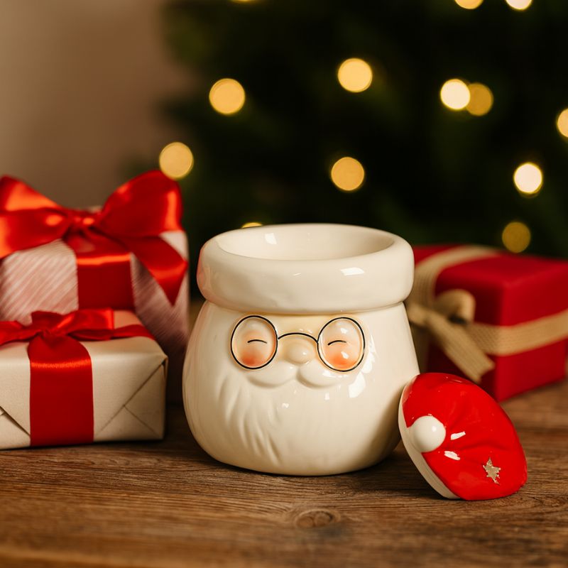 Brule Parfum Magie de Noël, le couvercle du bruleur est posé à côté de celui-ci, il y a des cadeaux autour et le tout est posé sur une table en bois. Esprit de Noël.