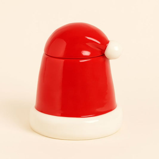 Brule Parfum Noël Rouge Magique, en forme de bonnet du père Noël et de couleur rouge et blanc. Sur fond beige clair.