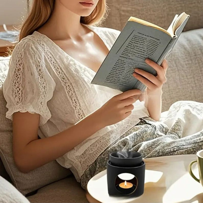 Brule Parfum Noir Prestige, posé sur une table basse en bois et une personne est assise sur un canapé à côté.