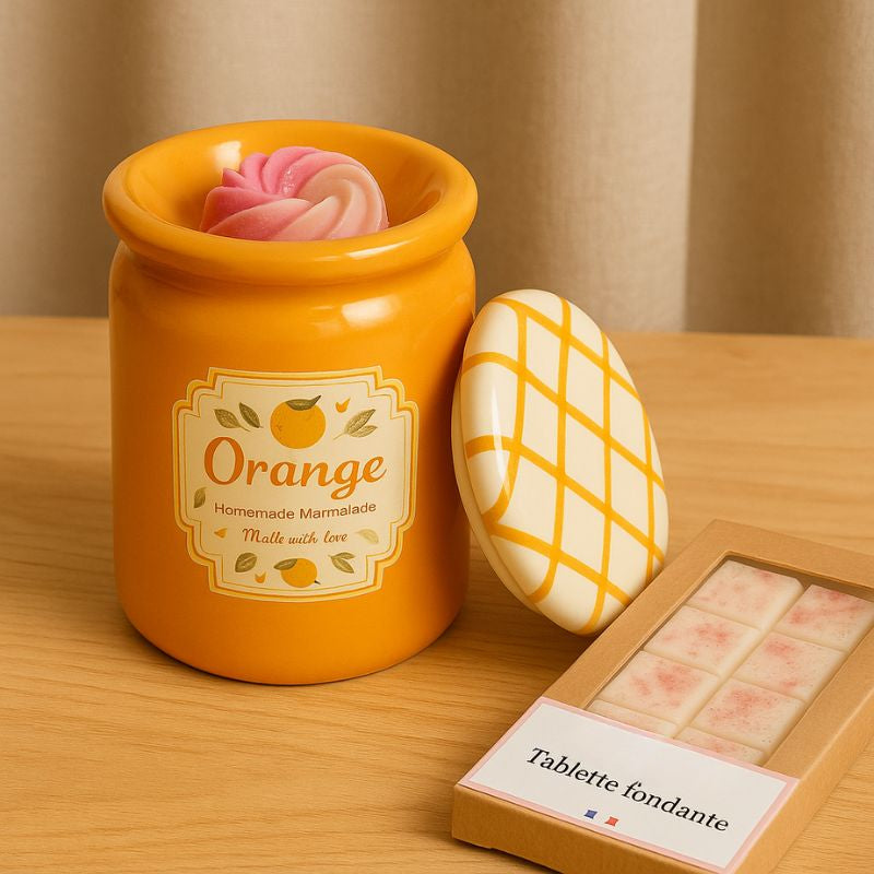 Brule Parfum Pot Délice d'Agrumes orange en céramique avec fondant parfumé dans la coupelle et tablette de fondants parfumés à côté sur table en bois.