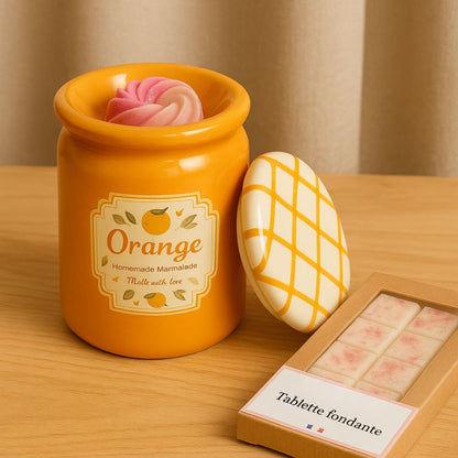 Brule Parfum Pot Délice d'Agrumes orange en céramique avec fondant parfumé dans la coupelle et tablette de fondants parfumés à côté sur table en bois.
