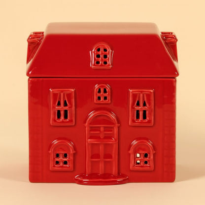Brule Parfum Rouge Chalet Enchanté en forme de maison rouge avec fenêtres ajourées, compatible fondants parfumés et bougie chauffe-plat et sur fond beige clair.