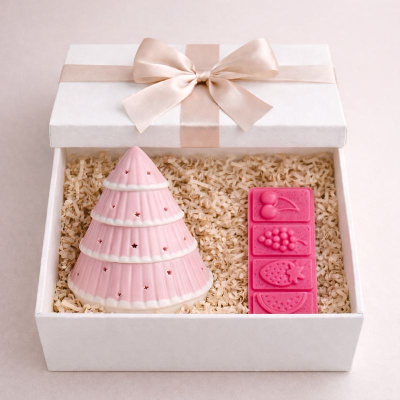 Brule Parfum Sapin Rose Féérique, il est dans un coffret caddeau avec un fondant parfumé en forme de barre et de couleur rose. Ambiance chaleureuse. Sur fond rose pale.