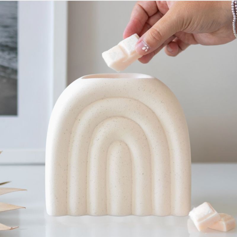 Brule Parfum XL Arc Déco Chic, une personne ajoute un fondant parfumé dans le brûleur, il est posé sur une table en marbre.