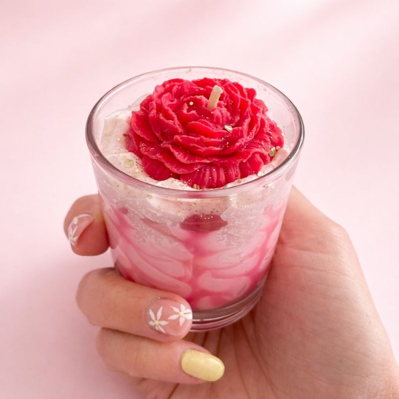 Bougie fleur artisanale rose tenue à la main dans un verre avec effet chantilly marbré.