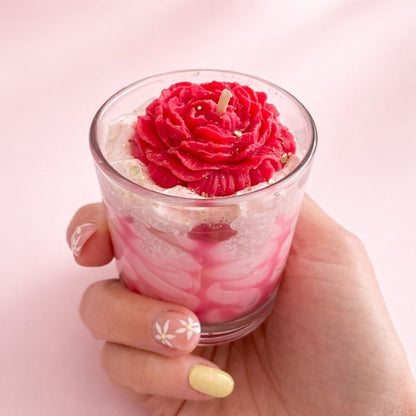 Bougie fleur artisanale rose tenue à la main dans un verre avec effet chantilly marbré.
