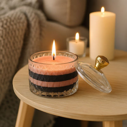Coffret Bougie Cire Perle, rose et noire en couches allumée dans bonbonnière en verre sur table décorative.