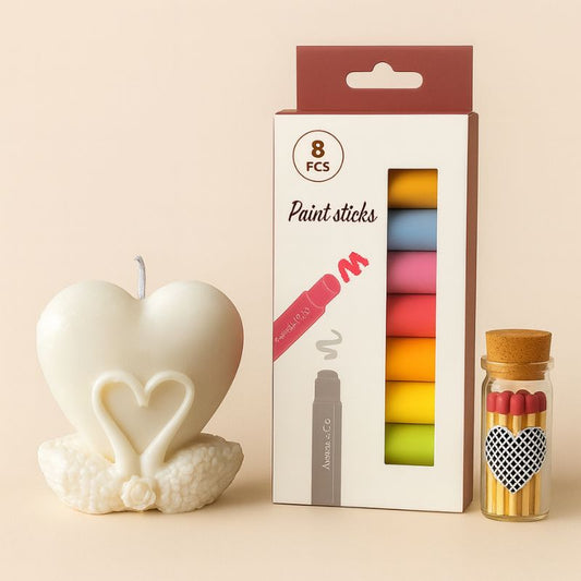 Coffret Bougie à Décorer Cœur Lunaire, bougie blanche en forme de cygne avec un cœur au milieu, des feutres en cire et des allumettes. Fond beige clair.