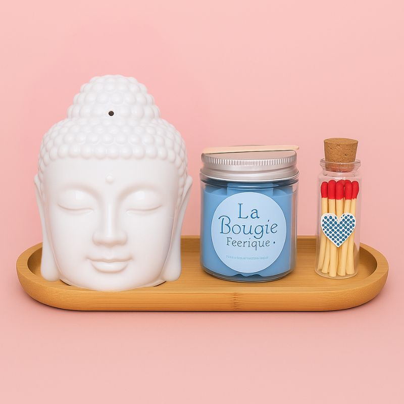 Coffret Bougie Douceur Scandinave, avec un bruleur Bouddha blanc, un fondant bleu, des allumettes et un plateau en bois. Sur fond rose clair.