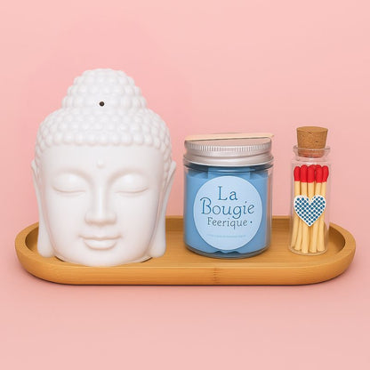 Coffret Bougie Douceur Scandinave, avec un bruleur Bouddha blanc, un fondant bleu, des allumettes et un plateau en bois. Sur fond rose clair.