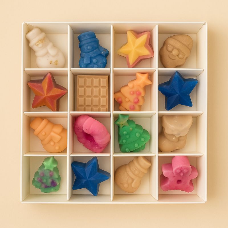 Coffret Bougie Édition Limitée Fondant Signature, la boite est ouverte pour voir tous les fondants parfumés à l’intérieur. Sur fond beige clair.