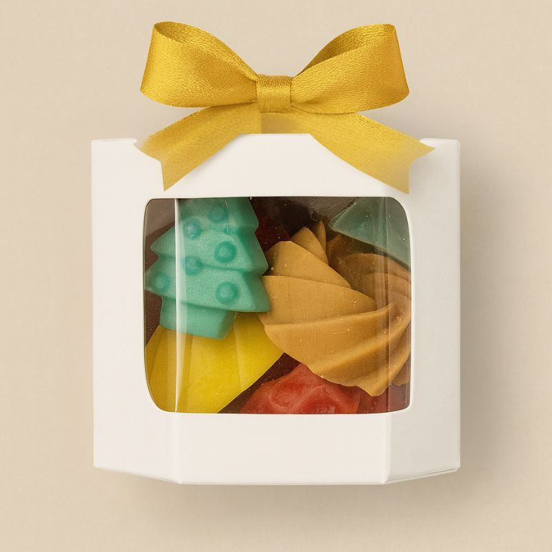 Coffret Bougie Fondant Parfumé Ambiance de Noël, avec plusieurs fondants dans la boîte de couleur blanche, avec un nœud doré sur le dessus et sur fond beige clair.