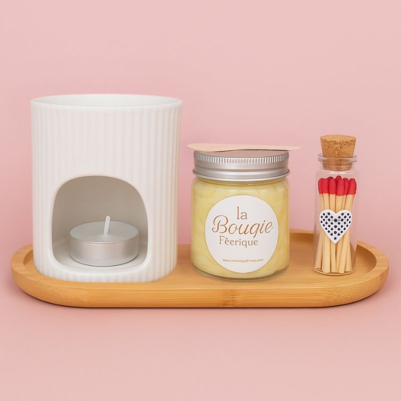 Coffret Bougie Rituel Féérique, avec un bruleur blanc, un fondant crémeux, une fiole avec des allumettes et un plateau en bois, le tout sur fond rose clair.