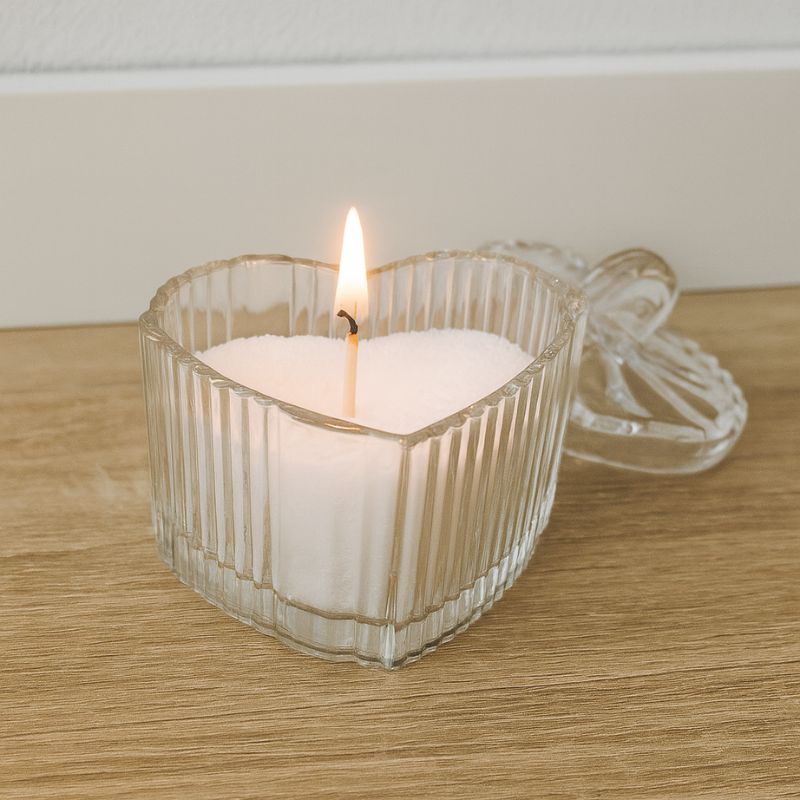Coffret Bougies Perles Rituel Cocooning, dans le contenant en verre y est déposé la cire perle blanche, avec la mèche qui est allumée. Posé sur une table en bois.