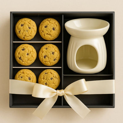 Fondant Parfumé Biscuit Cookie, présenté dans un coffret-cadeau noir avec un brule parfum à côté. Il y a un nœud sur la boîte. Sur fond beige clair.