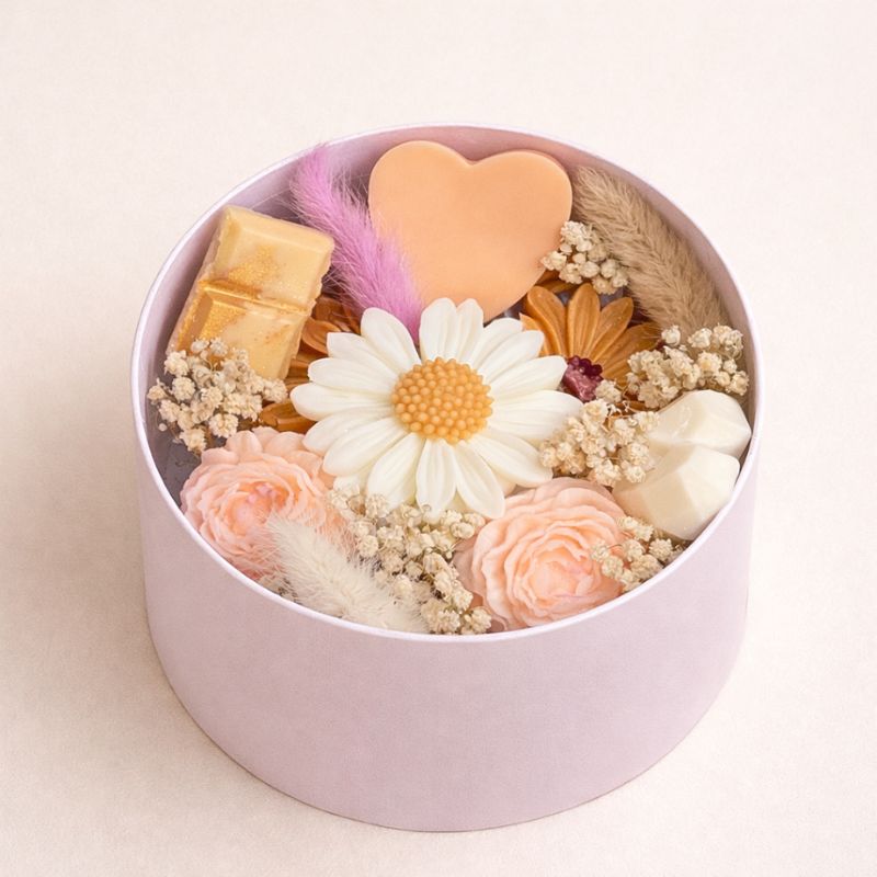 Fondant Parfumé Bouquet Signature en coffret rond rose avec fleurs décoratives et fondants en forme de marguerite, cœur et roses. Sur fond beige clair.