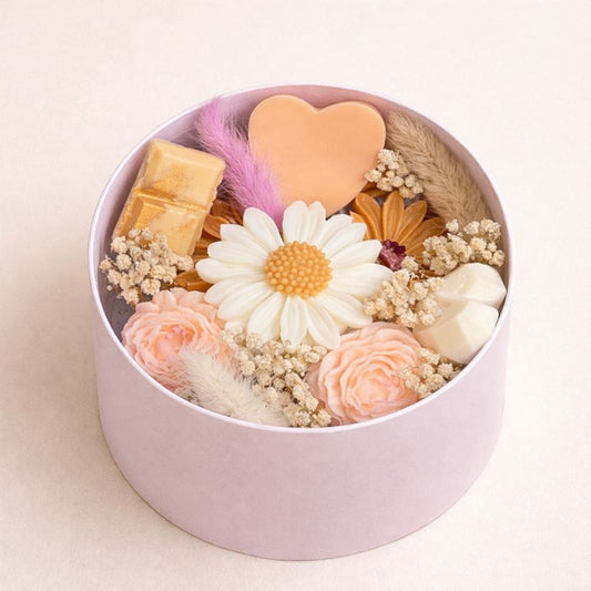 Fondant Parfumé Bouquet Signature en coffret rond rose avec fleurs décoratives et fondants en forme de marguerite, cœur et roses. Sur fond beige clair.