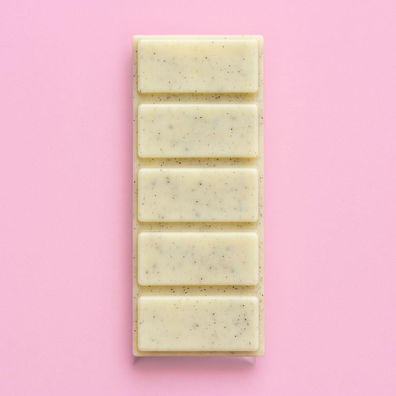 Fondant Parfumé Bûche de Noël Snapbar, de couleur jaune avec des paillettes, en forme de tablette et le parfum est bûche de Noël. Sur fond rose pâle.