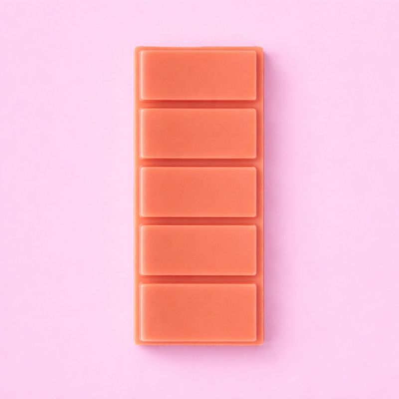 Fondant Parfumé Clémentine Monoï Snapbar, de couleur corail, format tablette sécable et sur fond rose.