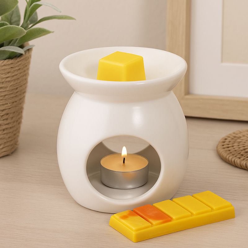 Fondant Parfumé Feu de Bois Snapbar, le fondant est présenté dans un brûleur blanc et allumé. Le reste de la barre de fondant parfumé est posé sur la table en bois. Ambiance cosy.
