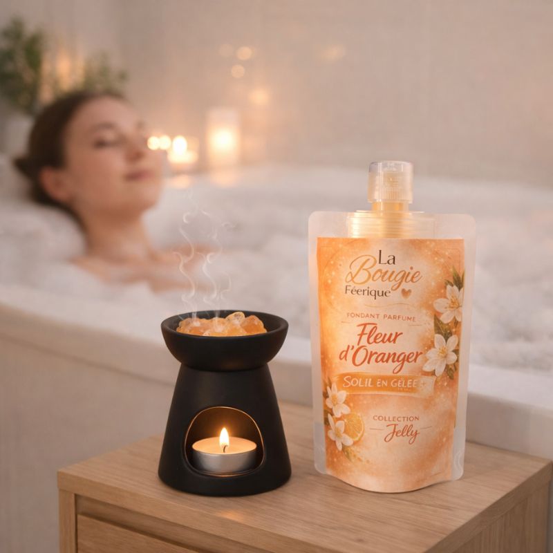 Fondant Parfumé Fleur d’Oranger gourde de fondant parfumé et brûle-parfum noir posés sur une table en bois, avec une personne dans un bain en arrière-plan flouté dans une ambiance chaleureuse.