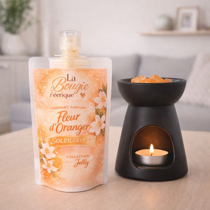 Fondant Parfumé Fleur d’Oranger gourde de fondant parfumé à côté d’un brûle-parfum noir allumé, posés sur une table en bois dans un intérieur lumineux et épuré.