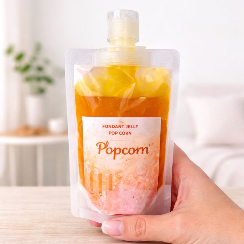 Fondant Parfumé Pop-Corn en gourde, texture gel orange visible, tenu en main, ambiance scandinave.
