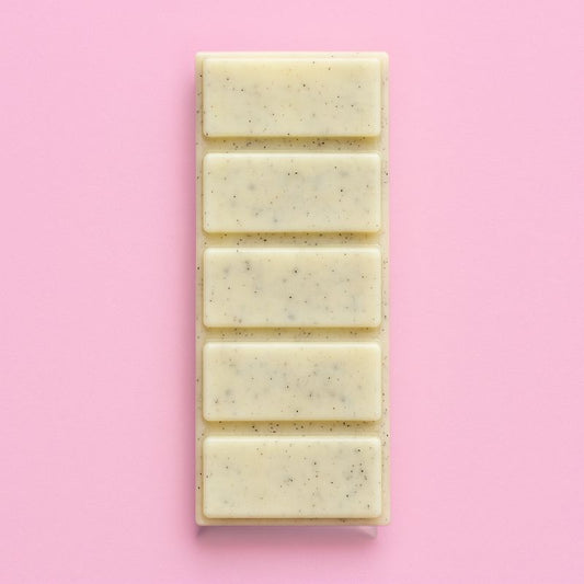 Fondant Parfumé Snapbar Bûche de Noël, de couleur jaune avec des paillettes, en forme de tablette et le parfum est bûche de Noël. Sur fond rose pâle.