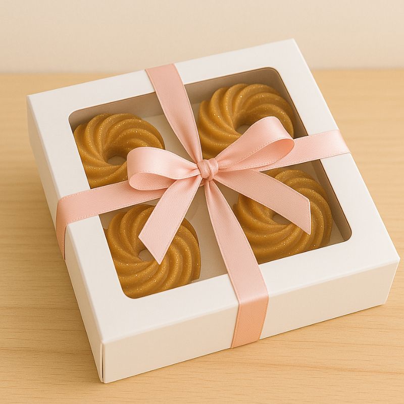 Fondant Parfumé Spirale Madeleine, présenté dans une boite-cadeau blanche avec un nœud rose. Fond beige.