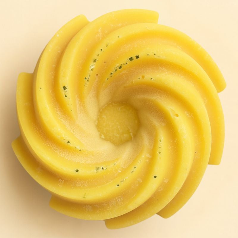 Fondant Parfumé Spirale Monoï, de couleur jaune avec des paillettes, de forme spirale et sur fond beige clair.